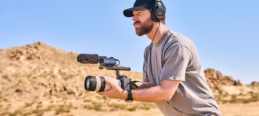 Изображение видеооператора в наушниках, использующего камеру FX5 с большим объективом и внешним микрофоном в пустыне.