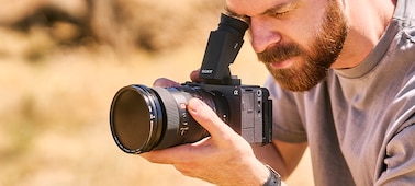 Изображение мужчины, который сидит на корточках на улице и смотрит через OLED-видоискатель VX7056, прикрепленный к камере FX5.